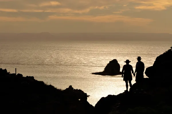 Pareja tomada de la mano sobre un risco mientras observa la puesta de sol durante un tour a la Isla Espíritu Santo.
