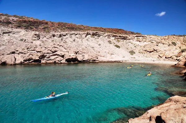 Panoramic view of a rocky cliff on Espíritu Santo Island with two people kayaking in crystal-clear waters