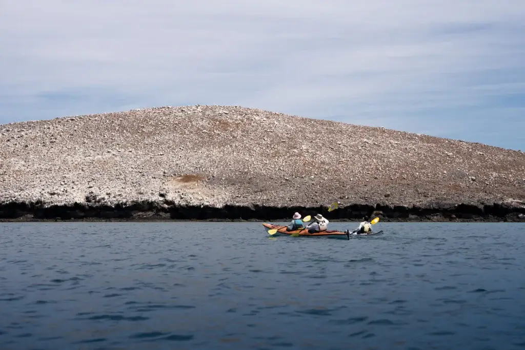 Coastal exploration Kayakers on the open water paddling past an imposing rocky islet under a bright midday sky