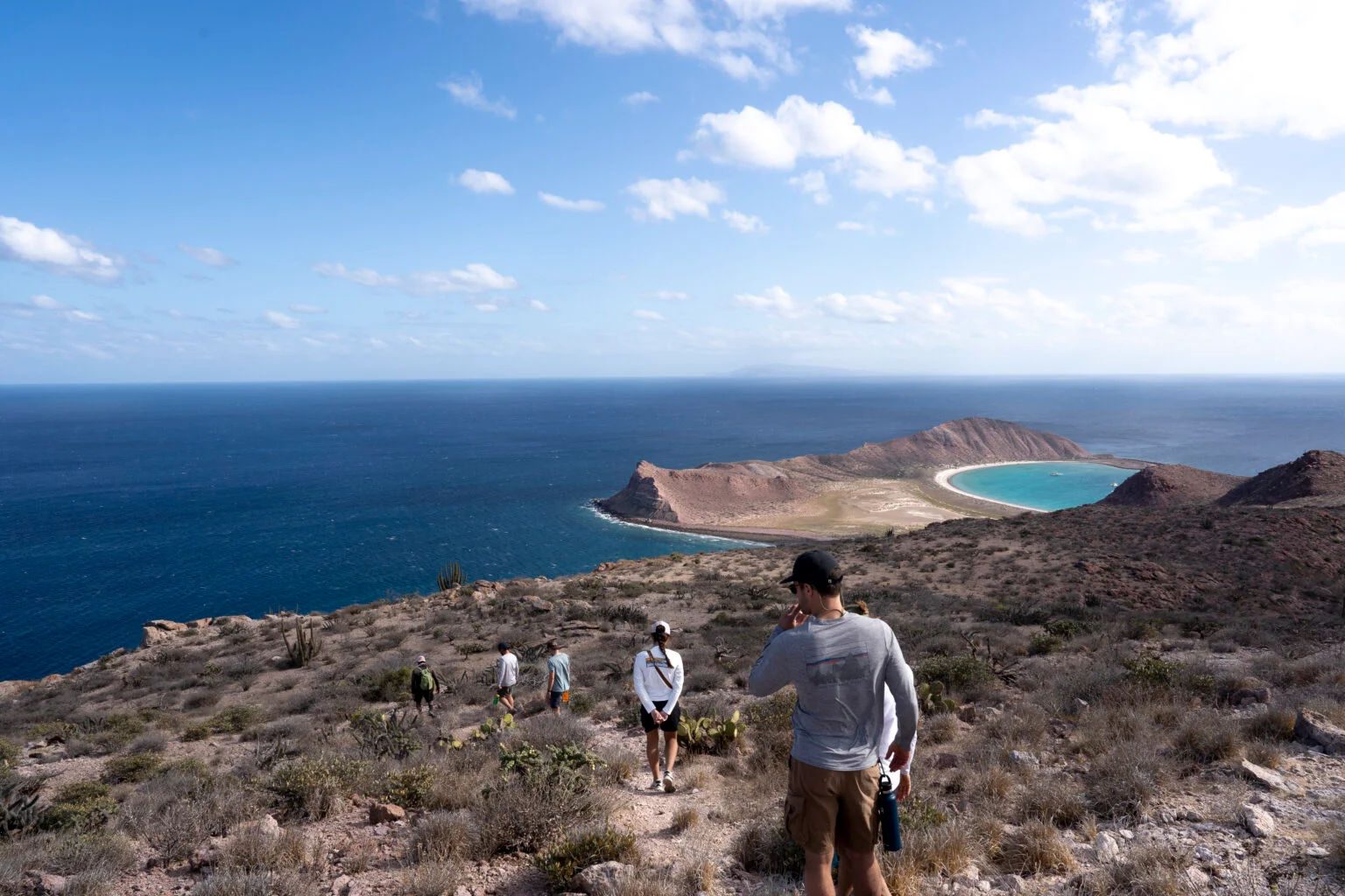 Grupo de senderistas en un terreno desértico con una vista espectacular de una bahía turquesa de la Isla San José en el Archipiélago San José