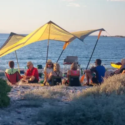 Campamento en la playa durante la tarde, personas conversando y disfrutando de la puesta de sol frente al mar, una de las cosas que hacer en Loreto México.